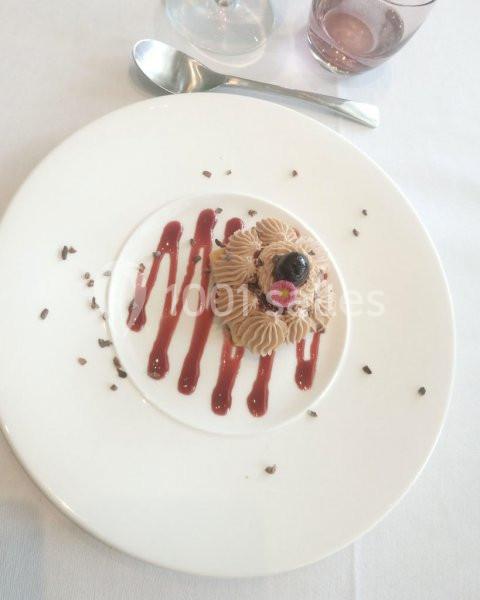 Dessert dressé sur une assiette blanche avec crème chocolatée, coulis rouge, éclats de cacao et décoration florale.