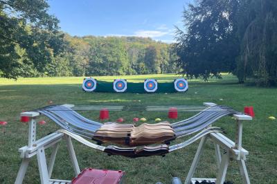 Maison blanche entourée d'arbres, avec terrasse équipée de parasols orange et mobilier de jardin en métal blanc.
