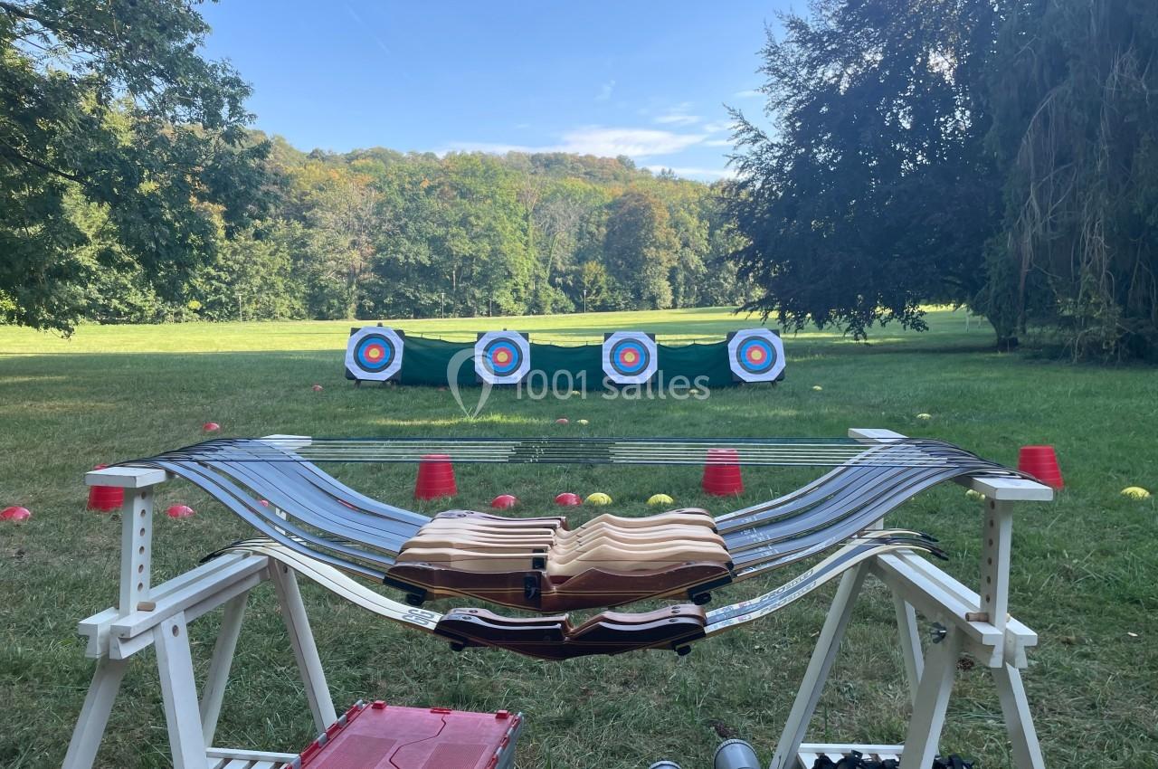 Quatre arcs posés sur un support devant une cible de tir à l'arc dans un champ verdoyant.