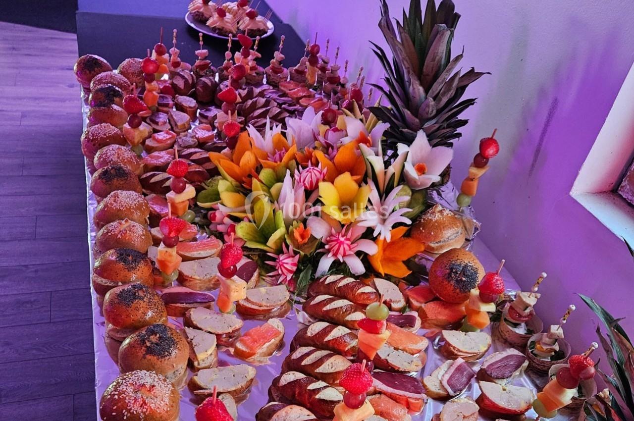 Buffet coloré avec pains, brochettes de fruits, charcuteries et décorations florales en fruits exotiques.