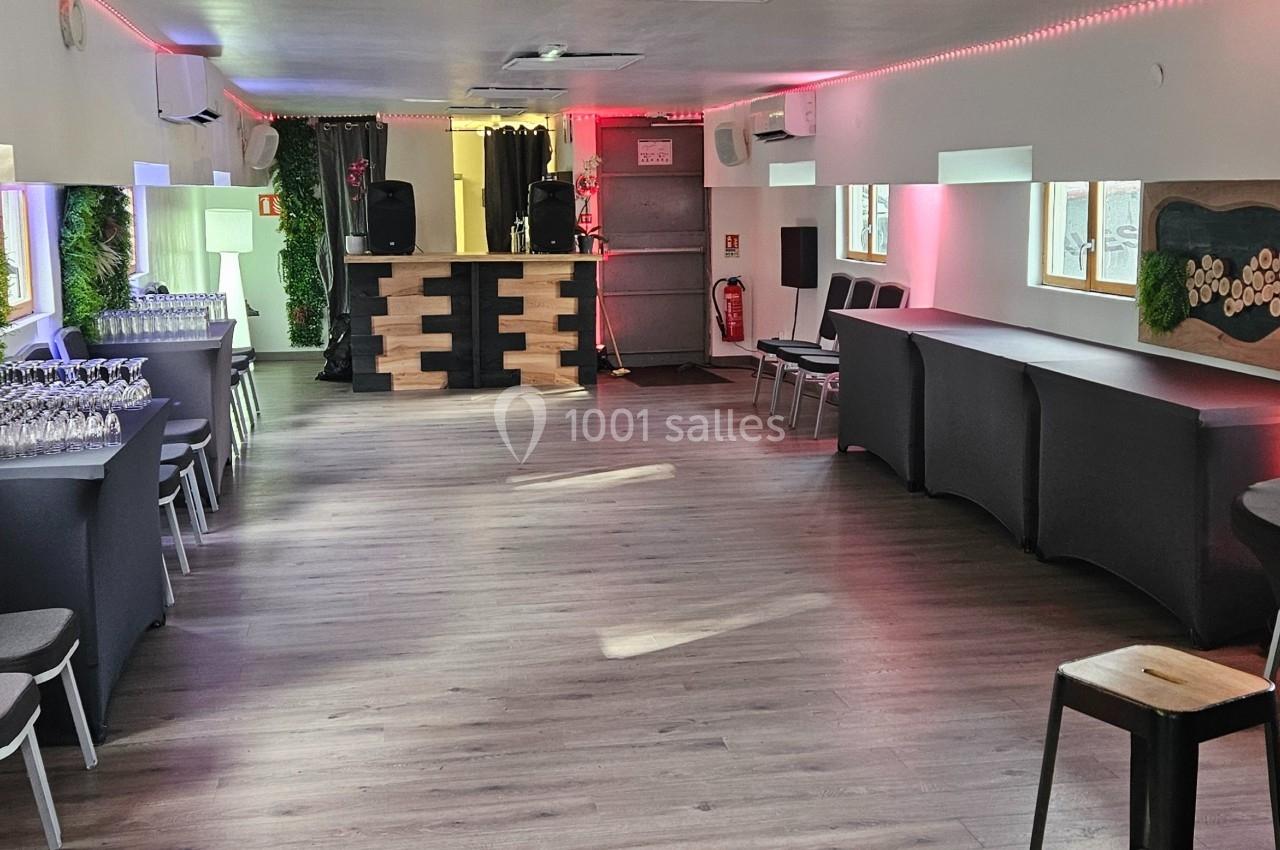 Salle lumineuse aménagée avec des tables hautes, chaises, décorations murales et un comptoir au fond.