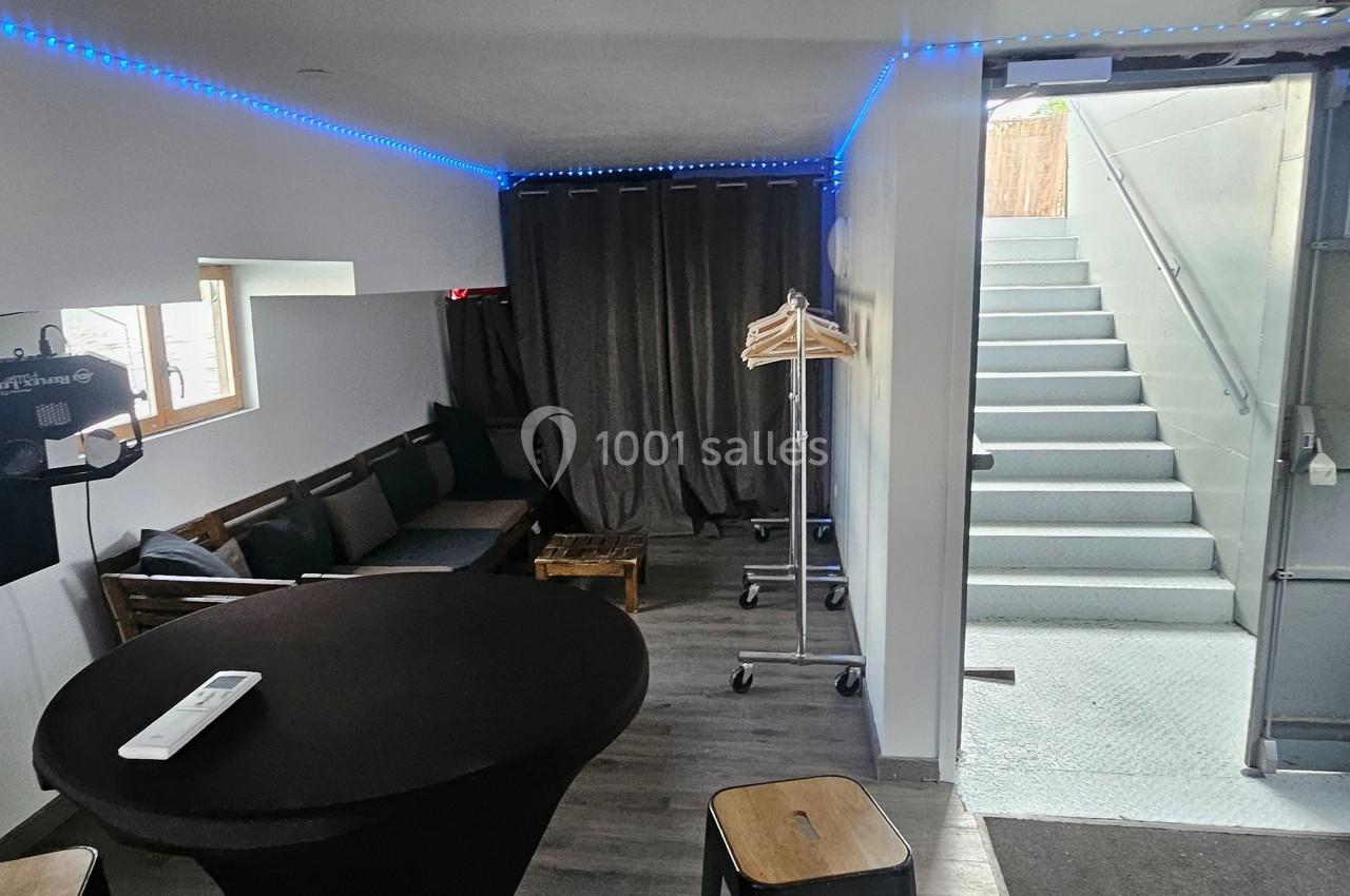 Espace intérieur avec table ronde, canapé, cintres, escalier menant à l'extérieur et éclairage LED bleu.