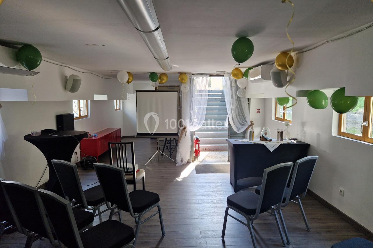 Salle décorée avec des ballons, équipée de chaises, d'un écran de projection et d'une table pour un événement.