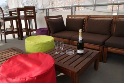 Salle lumineuse avec parquet clair, tables pliantes, chaises empilées et fenêtres laissant entrer la lumière naturelle.