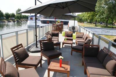 Salle lumineuse avec parquet clair, tables pliantes, chaises empilées et fenêtres laissant entrer la lumière naturelle.