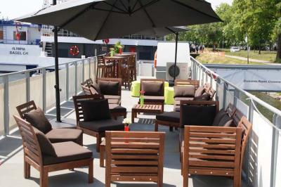 Salle lumineuse avec parquet clair, tables pliantes, chaises empilées et fenêtres laissant entrer la lumière naturelle.