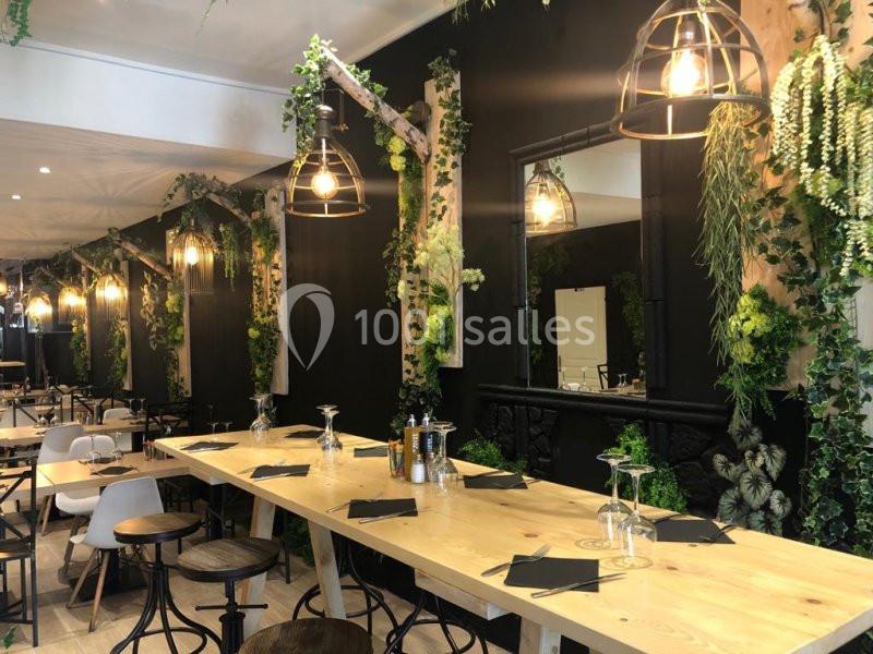 Salle de restaurant moderne avec tables en bois clair, décor végétal et luminaires suspendus.