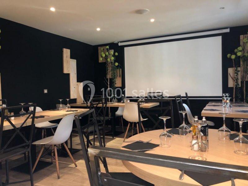 Salle de réunion ou de restauration avec tables rondes, chaises modernes et écran de projection en fond.