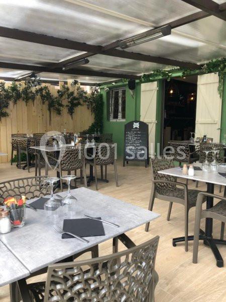 Terrasse d'un restaurant avec tables dressées, chaises en résine tressée, ardoise de menu et décor végétal.