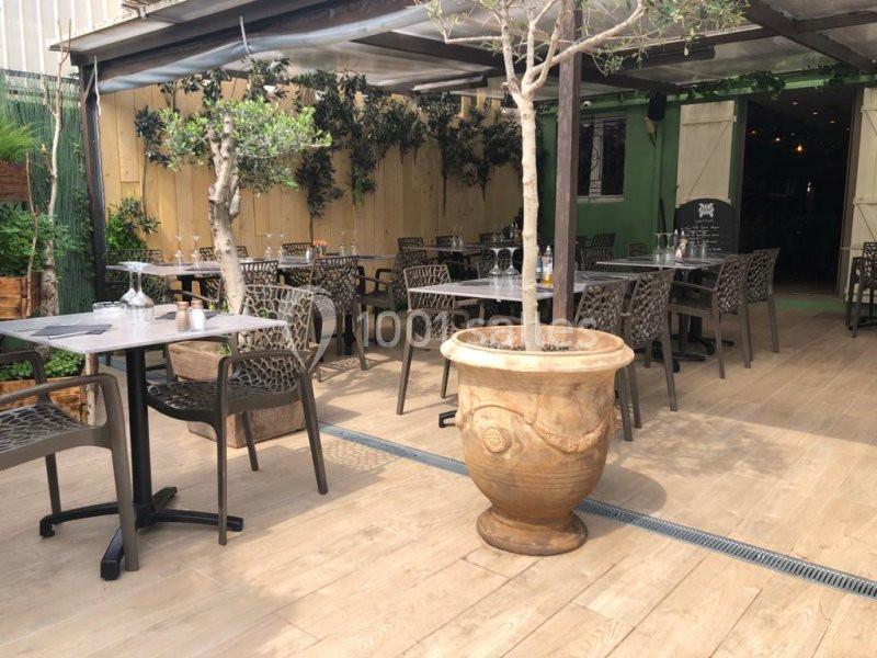 Terrasse extérieure avec tables dressées, chaises en métal ajouré, plantes et pergola partiellement couverte.