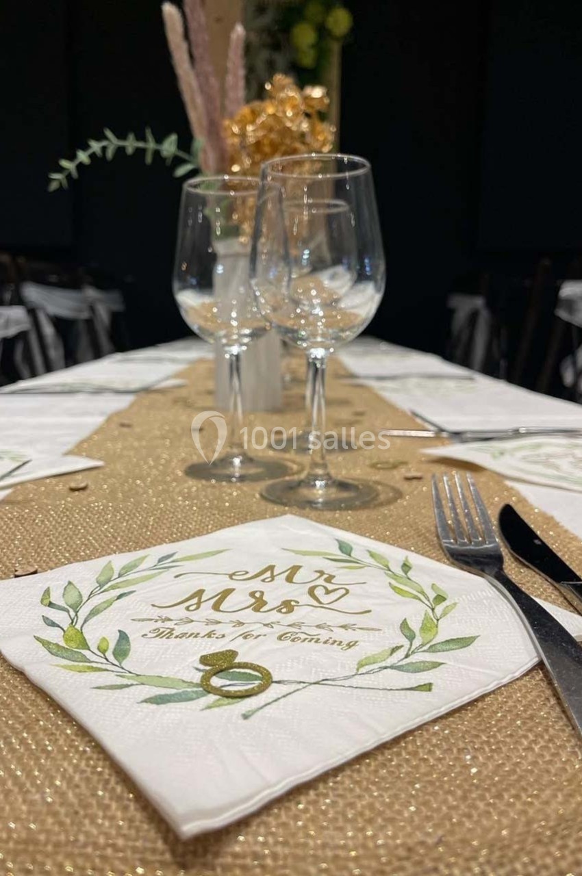 Serviette décorative avec inscription ’Mr & Mrs’ sur une table dressée avec nappe dorée, verres et décorations florales.