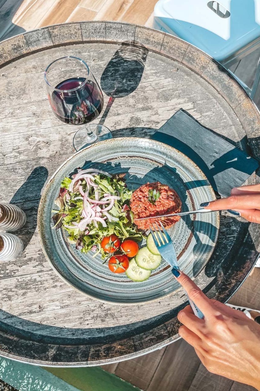 Assiette avec tartare de viande, salade verte, tomates cerises, rondelles de concombre, accompagnée d'un verre de vin rouge.