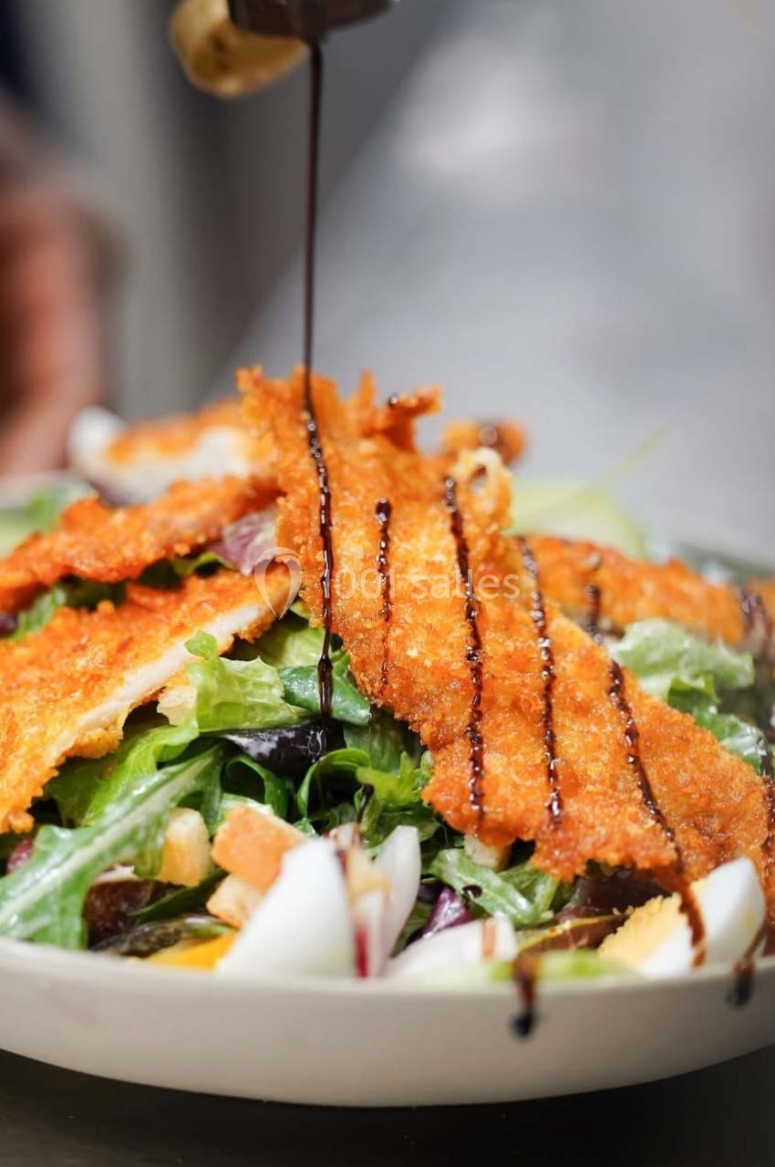 Salade garnie de filets de poulet panés, légumes frais et filet de sauce balsamique en cours de versement.