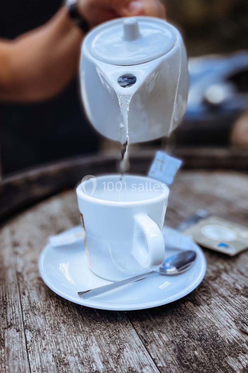 Une théière verse de l'eau chaude dans une tasse blanche posée sur une soucoupe avec une cuillère.
