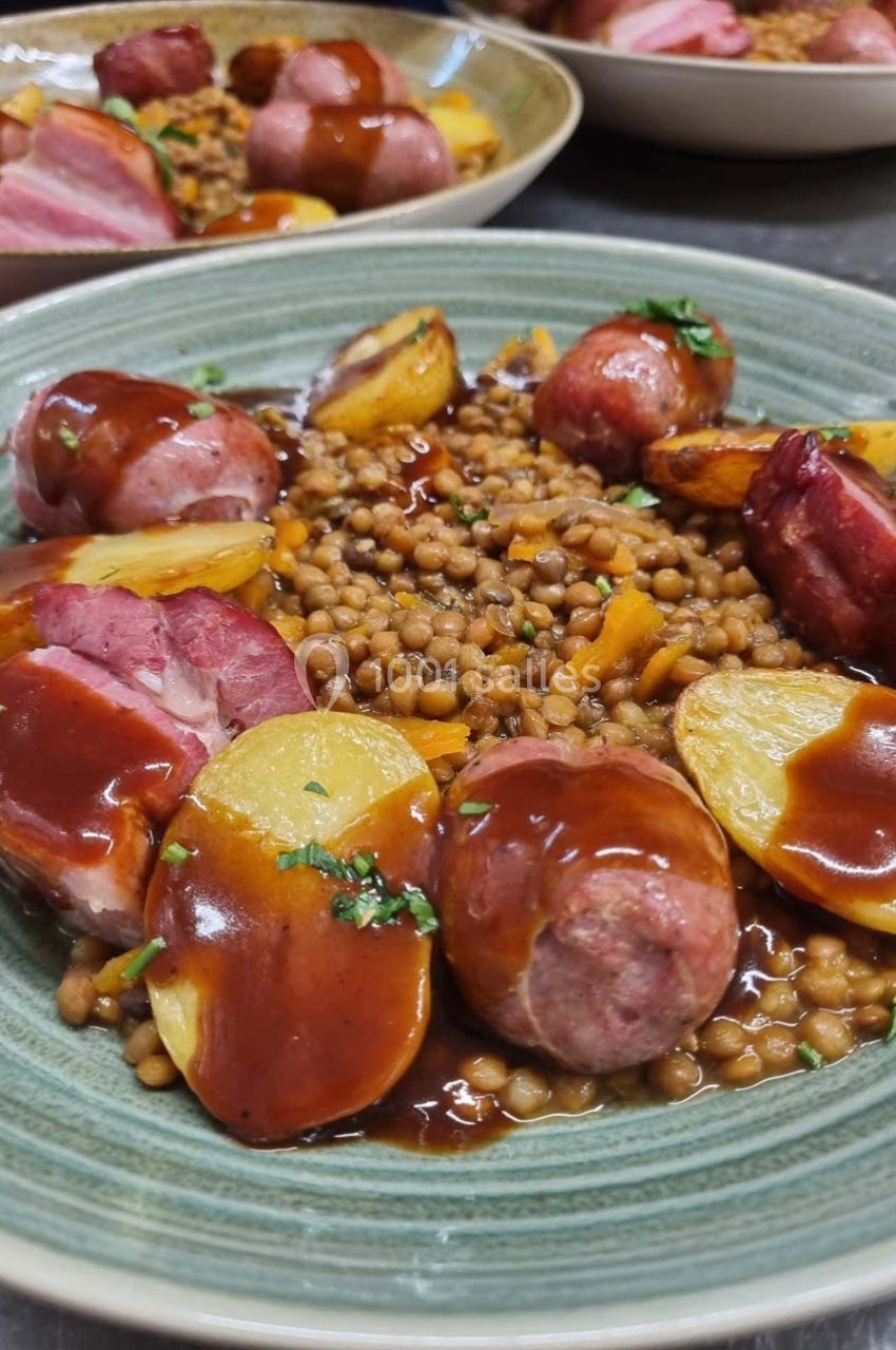 Assiette de lentilles garnie de saucisses, pommes de terre rôties et sauce, servie dans un plat en céramique.