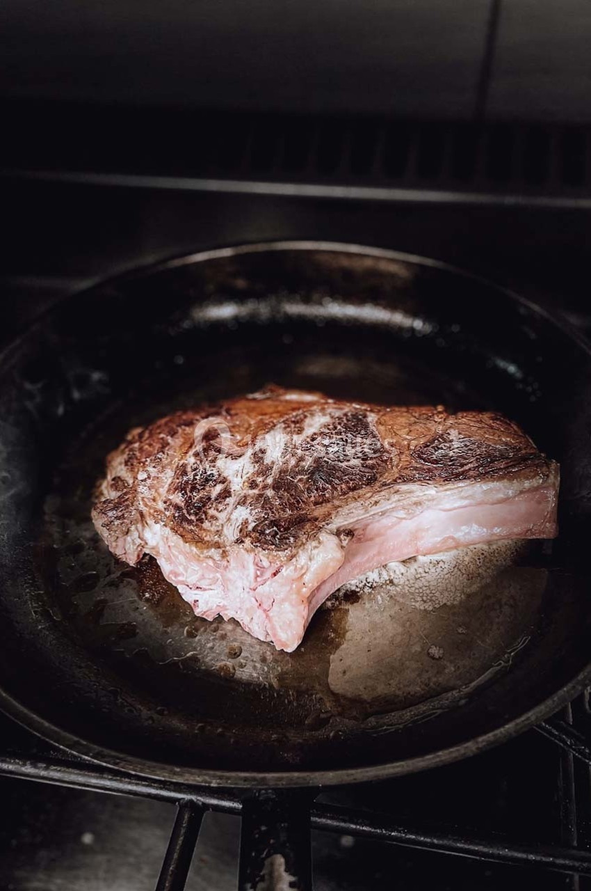 Bifteck épais en train de cuire dans une poêle en fonte sur une cuisinière.