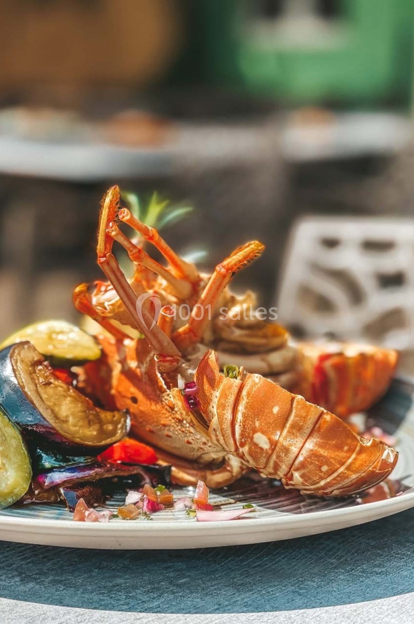 Assiette de langouste grillée accompagnée de légumes rôtis, servie en extérieur sur une table.