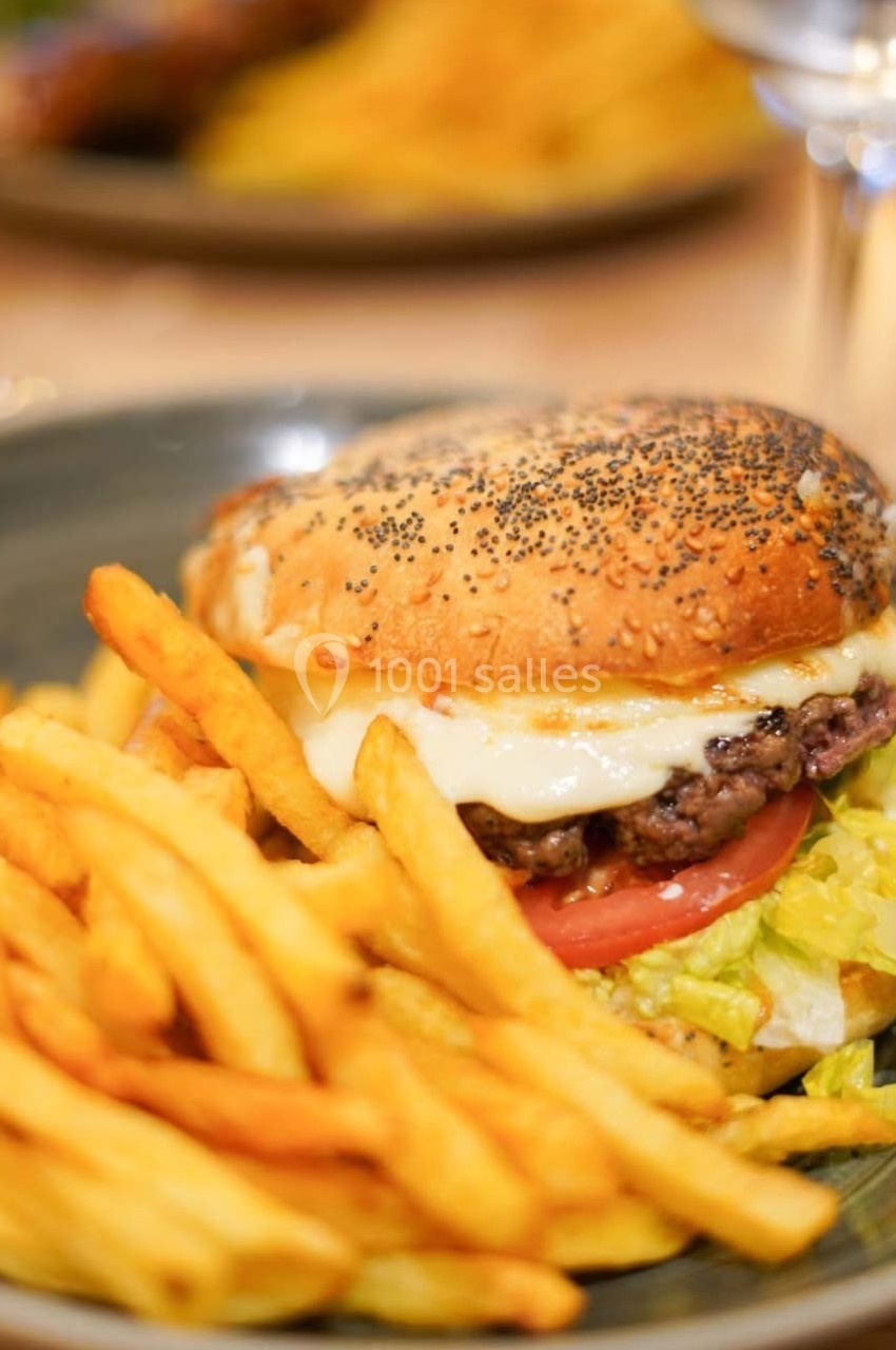 Burger au fromage avec salade et tomate, servi avec des frites dorées sur une assiette grise.