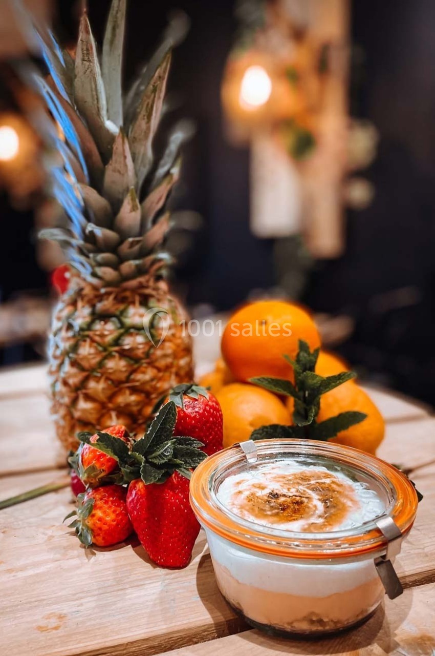 Dessert en verrine avec ananas, fraises et oranges disposés sur une table en bois dans un décor chaleureux.