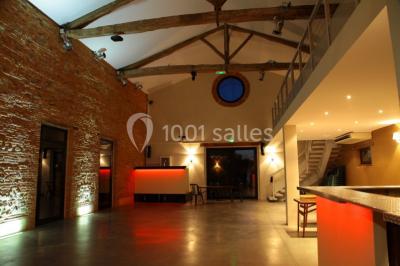 Salle spacieuse avec murs en briques, poutres apparentes, éclairage moderne et comptoirs lumineux rouges.