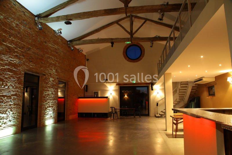 Salle spacieuse avec murs en briques, poutres apparentes, éclairage moderne et comptoirs lumineux rouges.