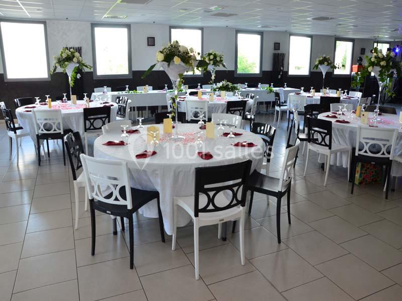 Salle de réception décorée avec des tables rondes dressées, nappes blanches, serviettes rouges et compositions florales.