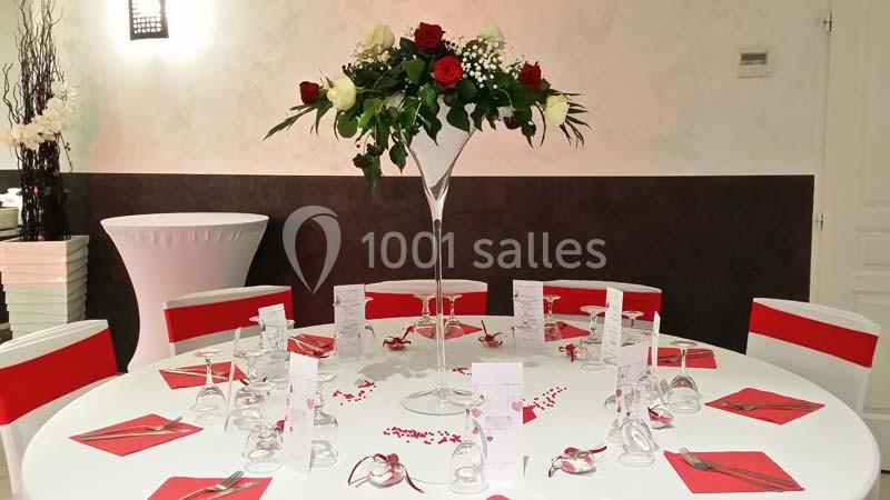 Table ronde décorée pour un événement, avec nappes blanches, chaises rouges, centre de table floral et menus disposés.