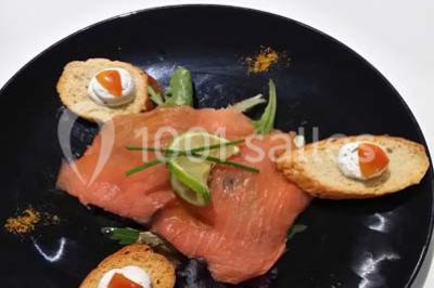 Assiette de saumon fumé avec tranches de citron vert, toasts garnis de crème et tomate, présentée sur un fond noir.