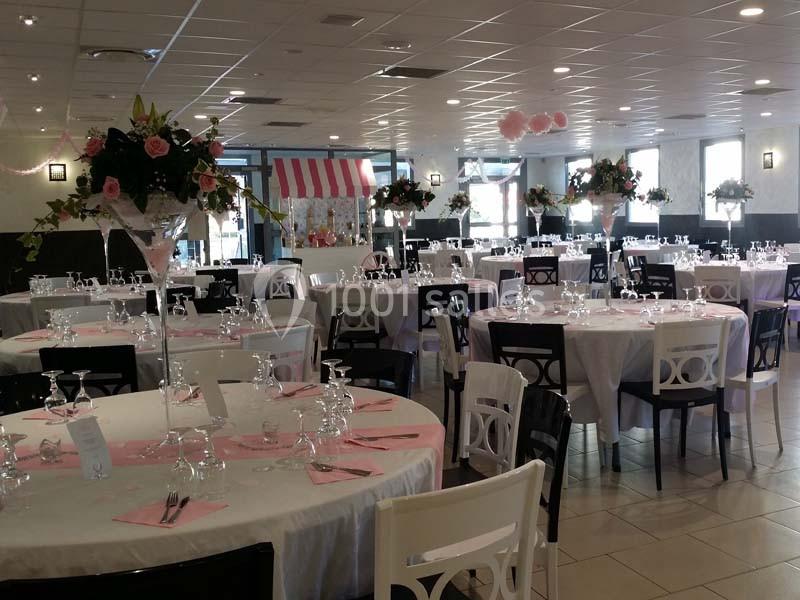 Salle de réception décorée avec des tables rondes, nappes blanches, accents roses et arrangements floraux élégants.