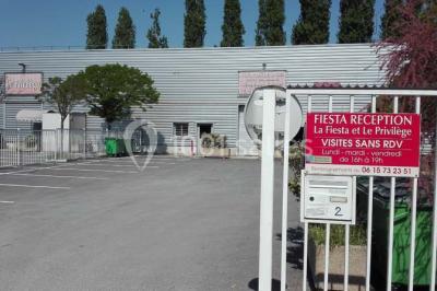Parking vide avec marquages au sol, entouré de bâtiments industriels et d'arbres sous un ciel dégagé.