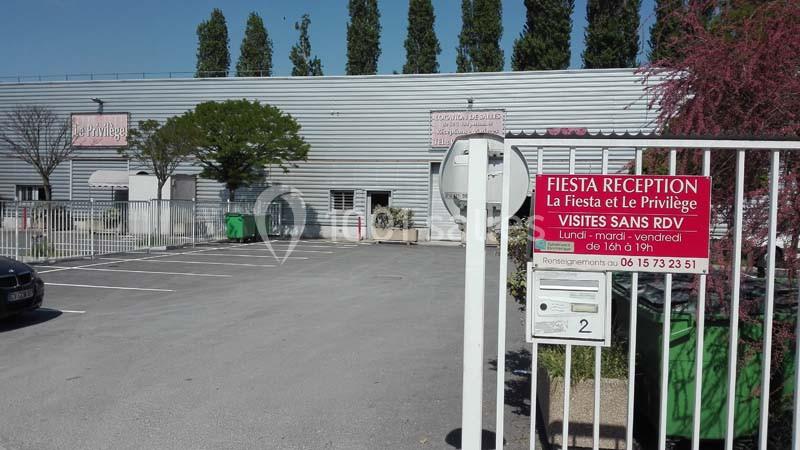 Entrée d'un parking devant un bâtiment gris avec des panneaux indiquant ’Fiesta Réception’ et horaires de visite.