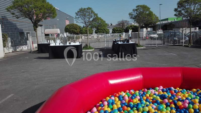 Piscine à balles colorées au premier plan dans un parking avec des tables dressées en arrière-plan.
