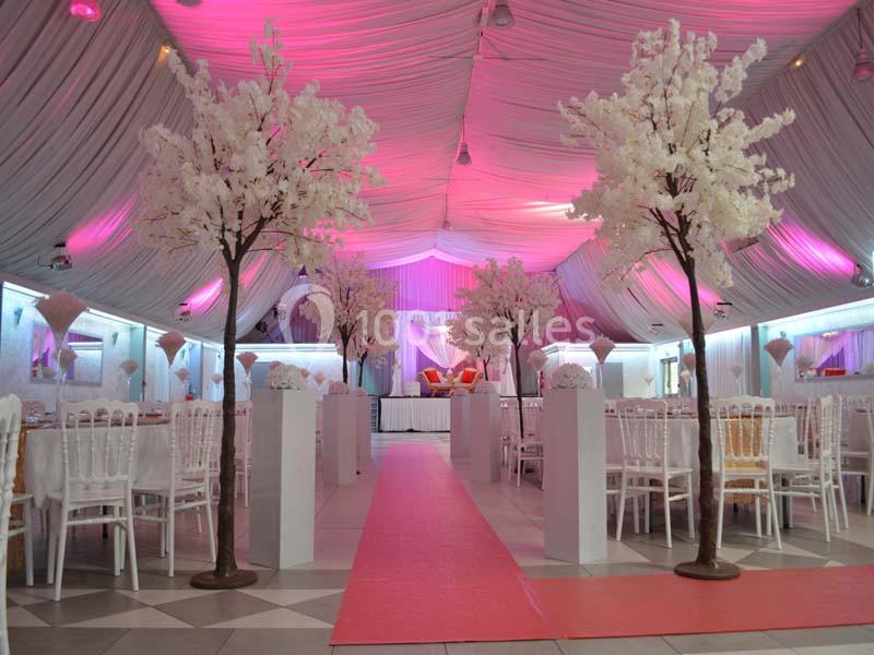 Salle de réception décorée avec des arbres artificiels blancs, un tapis rouge central et un éclairage rose.