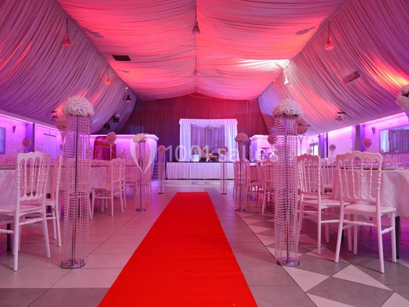 Salle de réception décorée avec des chaises blanches, des colonnes ornées de fleurs et un tapis rouge central.