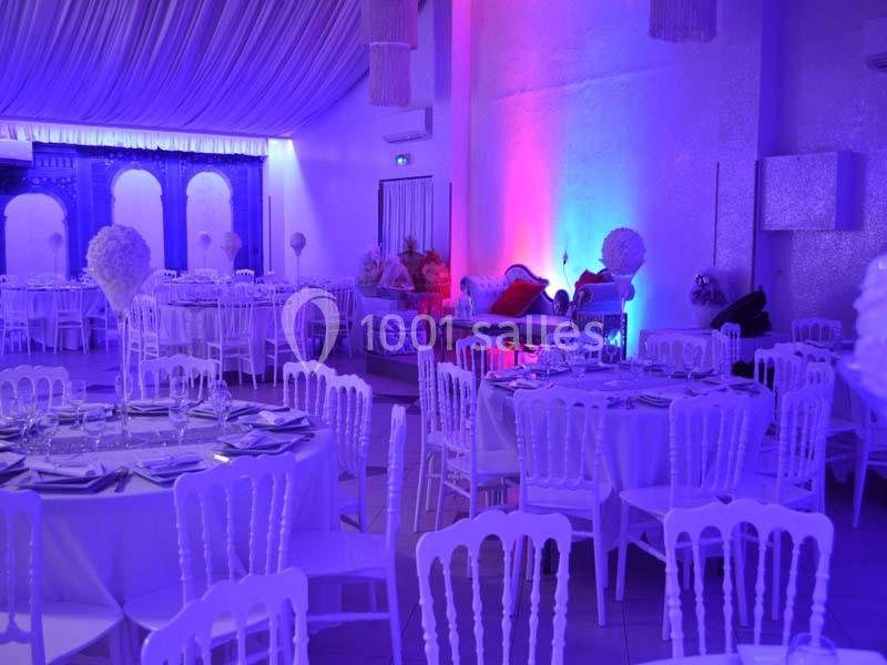 Salle de réception décorée avec des tables rondes, chaises blanches et éclairage coloré bleu et violet.