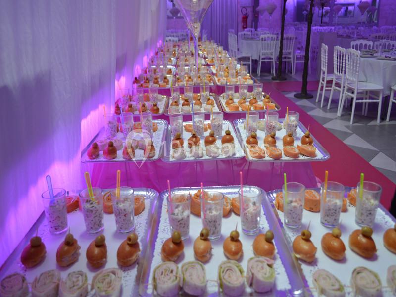 Buffet de verrines, mini-sandwichs et roulés disposés sur des plateaux dans une salle éclairée de lumières violettes.