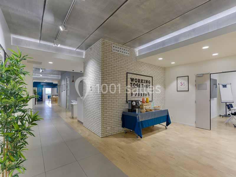 Espace intérieur lumineux avec mur en briques, table de collation et plantes, menant à une salle de réunion.
