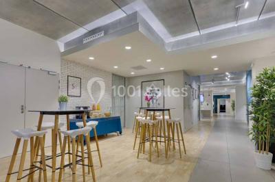 Terrasse avec des tables et chaises bleues, entourée de jardinières et d'une structure métallique végétalisée.