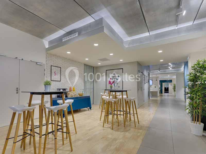 Espace lumineux avec tables hautes, chaises blanches, plantes et décorations murales dans un intérieur moderne.