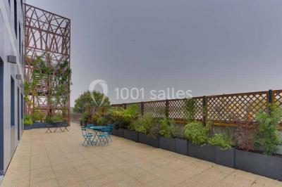 Terrasse avec des tables et chaises bleues, entourée de jardinières et d'une structure métallique végétalisée.