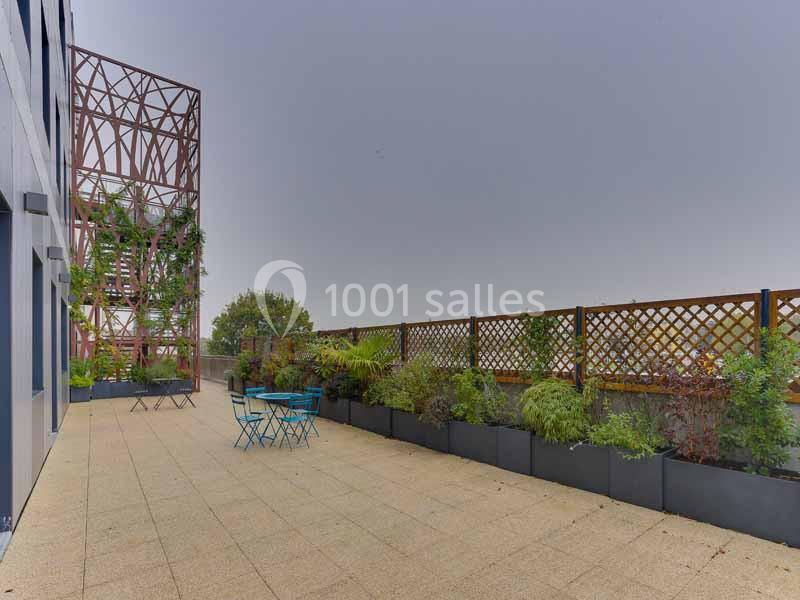 Terrasse avec des tables et chaises bleues, entourée de jardinières et d'une structure métallique végétalisée.