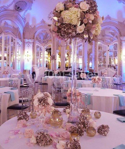 Salle de réception élégante avec tables décorées de fleurs pastel, chandeliers et centres de table raffinés.