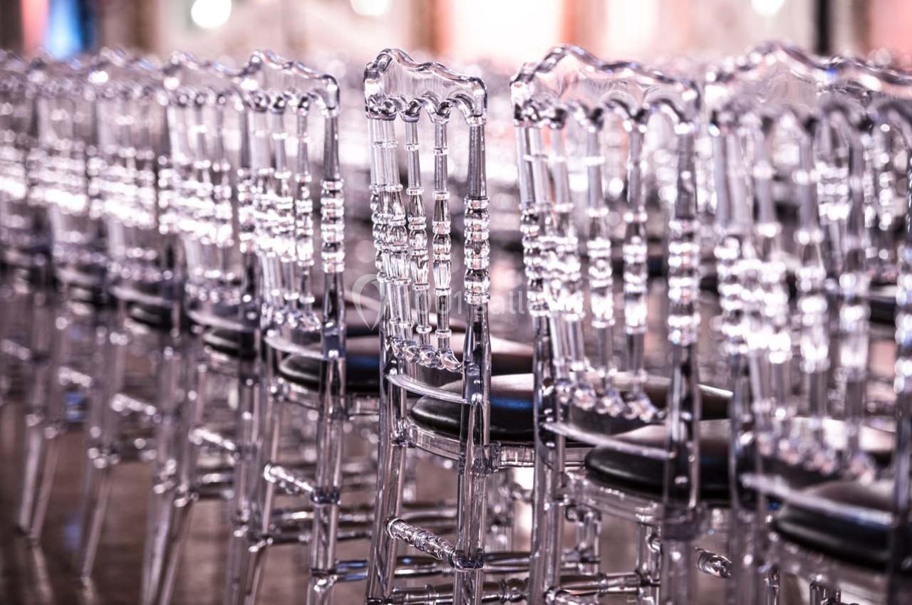Rangée de chaises transparentes alignées dans une salle lumineuse avec un sol réfléchissant.