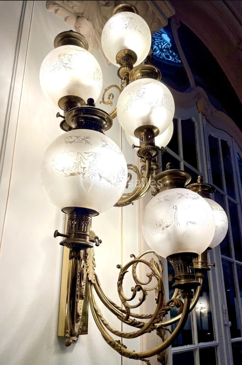 Applique murale en laiton avec globes en verre gravé, éclairant un intérieur aux moulures et grandes fenêtres.