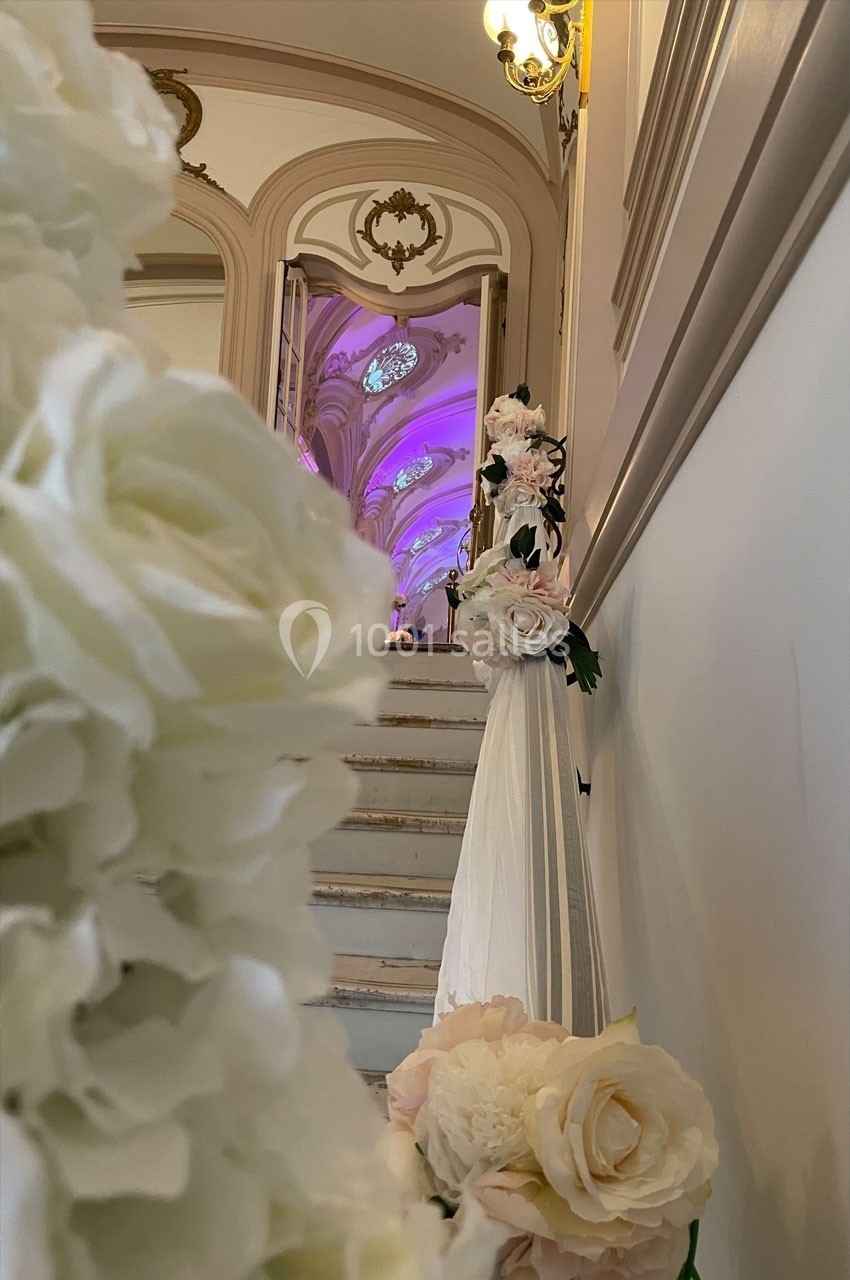 Escalier décoré de fleurs blanches et roses menant à une salle illuminée de lumières violettes.