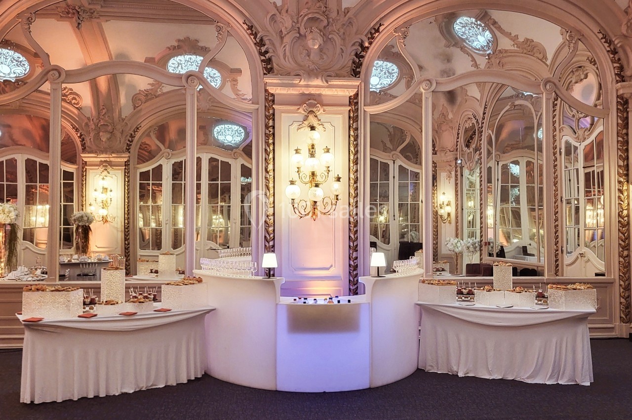 Salle de réception élégante avec miroirs ornés, lustre central et tables dressées pour un buffet.