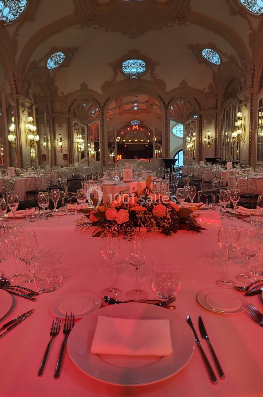 Salle de réception élégante avec tables dressées, nappes blanches, vaisselle raffinée et éclairage tamisé rouge.