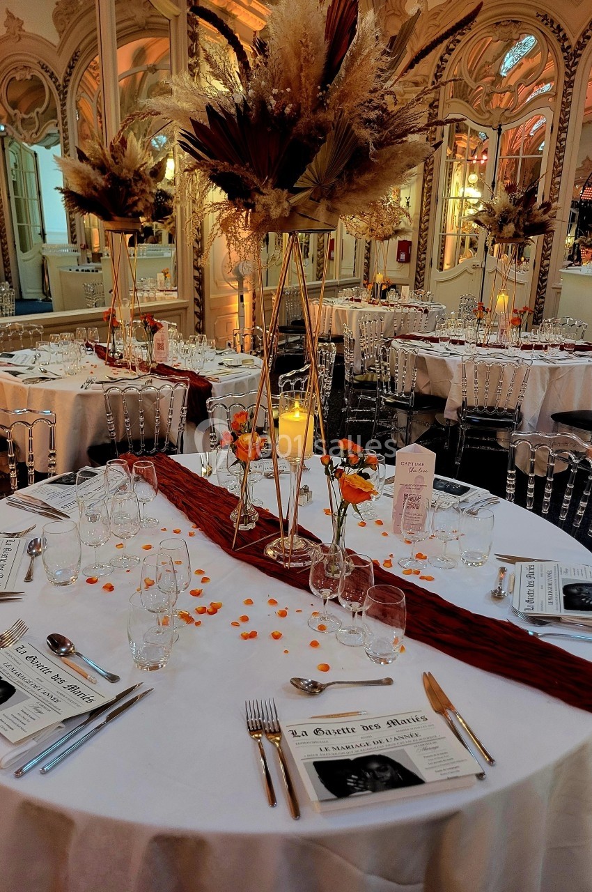 Salle de réception élégante avec tables rondes dressées, décor floral raffiné et ambiance lumineuse chaleureuse.