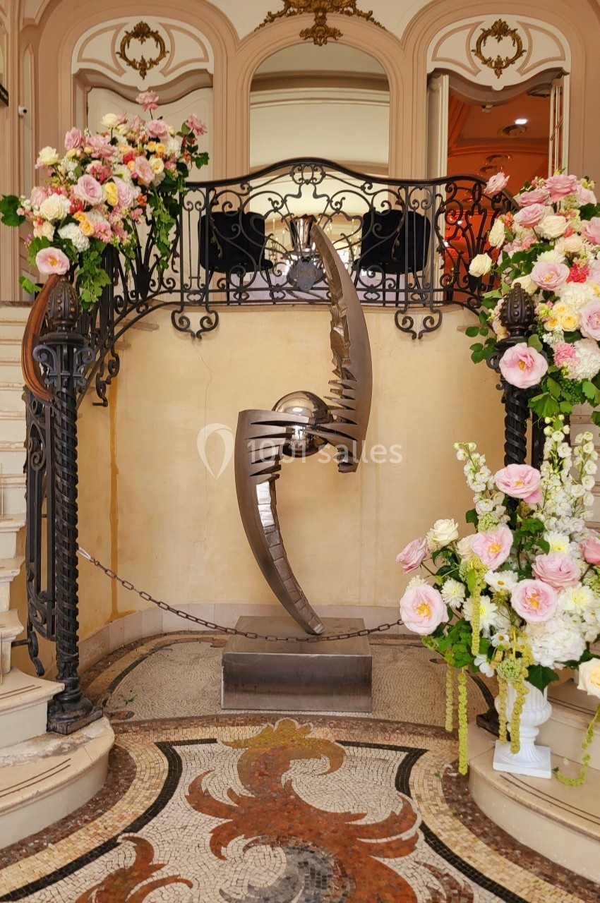 Sculpture métallique moderne entourée de bouquets de fleurs et encadrée par un escalier dans un décor élégant.