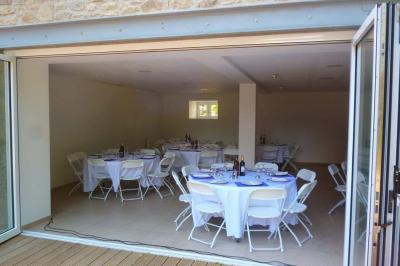 Jardin verdoyant avec un ruisseau traversant, entouré de grandes feuilles et d'arbustes fleuris, près d'une maison en pierre.